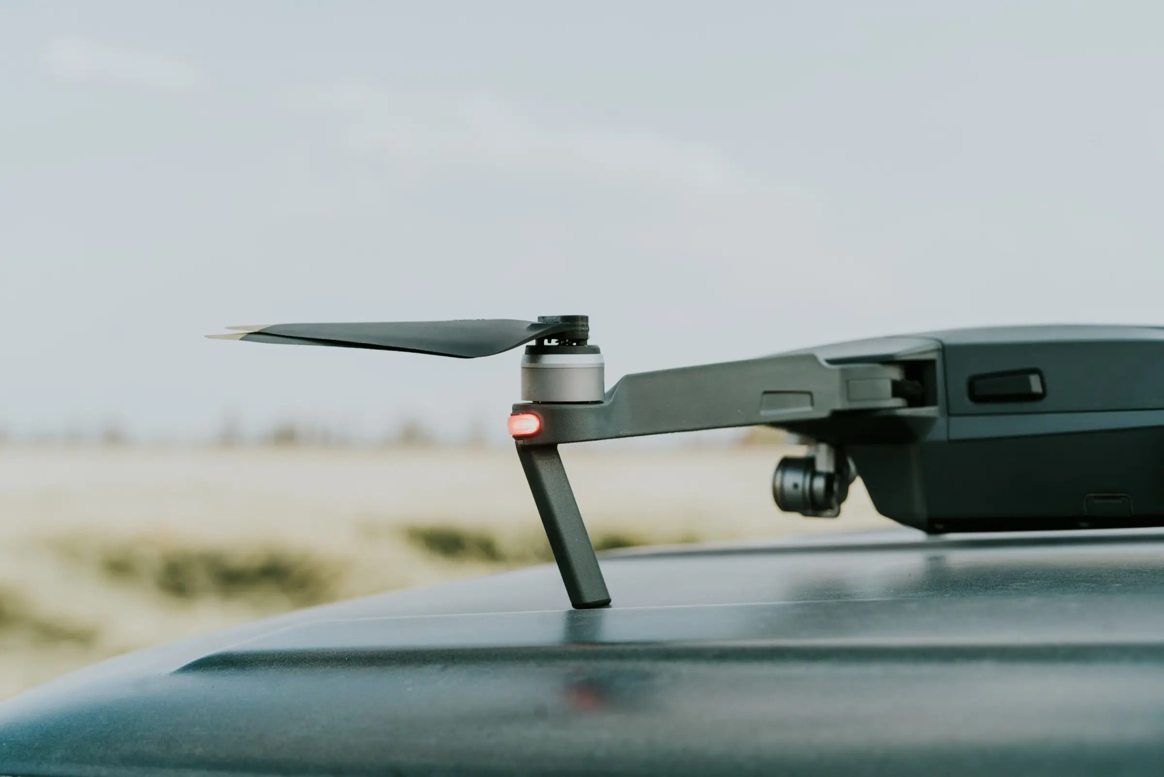 Side view of a folding drone's arm, motor and propeller, resting on a dark surface under a pale sky.